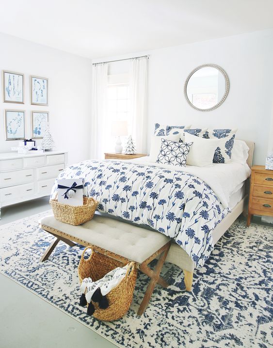 a white bedroom spruced up with blue and white textiles, with a blue and white gallery wall, a white dresser, a bed with printed bedding and a rug