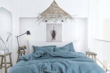 a white boho beach bedroom with all-white everything, blue bedding, baskets, a wicker lamp and wooden furniture