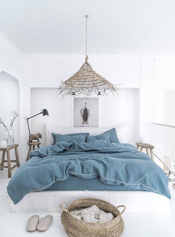 a white boho beach bedroom with all-white everything, blue bedding, baskets, a wicker lamp and wooden furniture