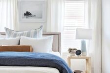an airy modern beach bedroom with neutral walls, white curtains, blue textiles and lamps, catchy dark items
