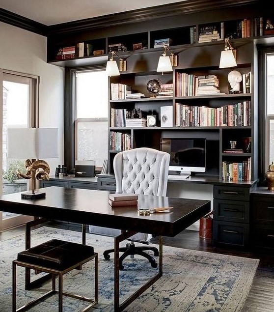 An elegant and chic masculine home office with a wooden desk and a stool, a built in bookcase and much natural ligjt