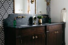 an elegant bathroom with a geo print wall, a double dark-stained vanity with a black stone countertop and elegant sconces