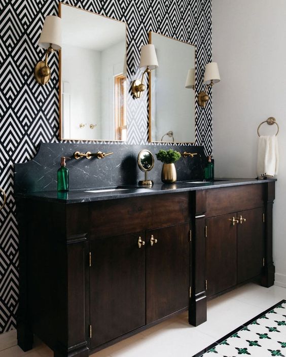 An elegant bathroom with a geo print wall, a double dark stained vanity with a black stone countertop and elegant sconces