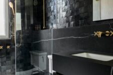an elegant black bathroom with Zellige tiles, a shower space, a toilet, a fluted vanity with a black slab sink