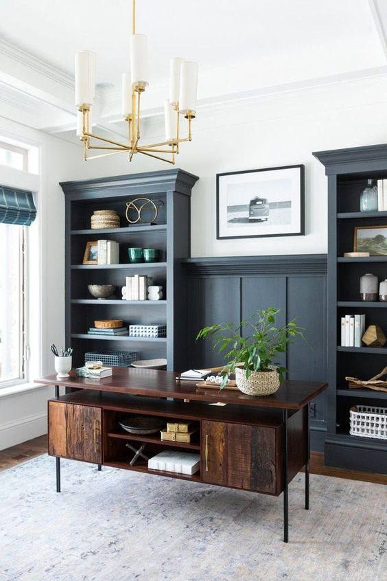 An elegant home office with graphite grey built in shelves, a dark stained desk and some decor plus a chic chandelier