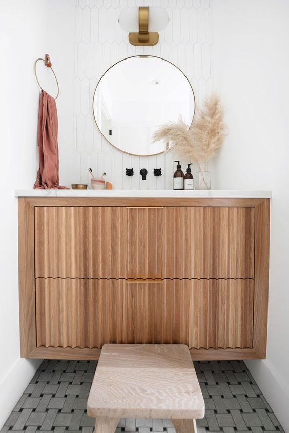 an elegant stained reeded vanity with a stone countertop, white tiles, a round mirror and black fixtures and a cool sconce