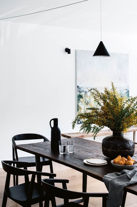 An exquisite modern dining space with a dark stained reclaimed table and black chairs, a pendant lamp and some blooms
