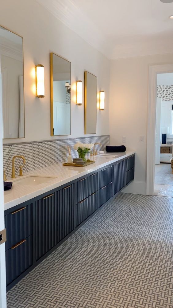an exquisite navy fluted vanity with a white stone countertop, gold fixtures and a series of mirrors is amazing