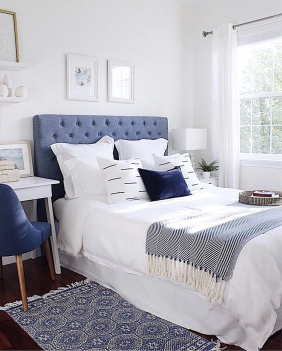 An eye catching bedroom with a blue bed, blue and white bedding, a printed rug, a white desk and a navy chair