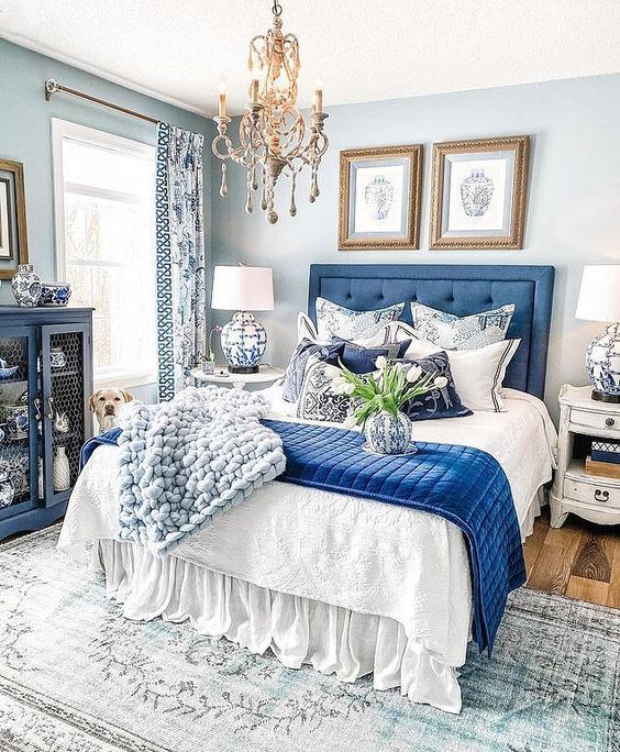 an eye-catching bedroom with light blue walls, a navy bed with navy and white bedding, a navy storage unit, printed curtains