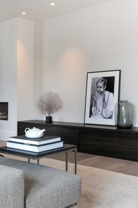 An ultra minimal living room with a dark stained storage unit, a grey sofa, a black table and a statement artwork