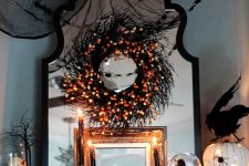 Hallowene mantel decor with black cheesecloth, a black garland with lights, a candy corn wreath, glitter pumpkins, black candles
