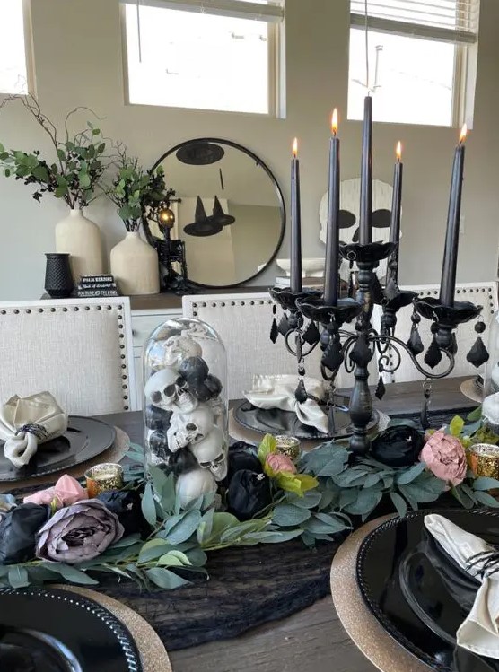 a Halloween centerpiece of a refined black candelabra with candles, skulls in a cloche and some fabric blooms