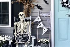 a Halloween porch with bats, a bunting, a skeleton rocking, cron husks and a skull wreath on the door is a cool idea