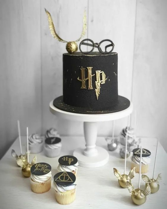 a Harry Potter sweets table with cupcakes, cake pops shaped as Snithces, a black and gold cake with glasses and a Snitch