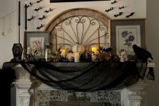 a beautiful Halloween fireplace styled in a classic way, with black cheesecloth, black candles, white pumpkins and candles, black bats on the wall