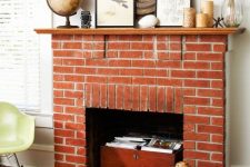 a beautiful non-working red brick fireplace with a chest with books, a stained mantel with candles and artworks and a globe
