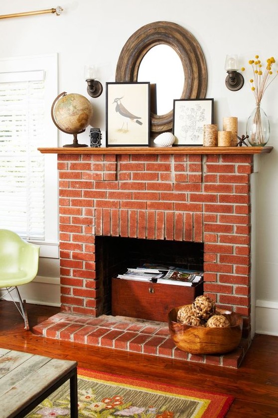 A beautiful non working red brick fireplace with a chest with books, a stained mantel with candles and artworks and a globe