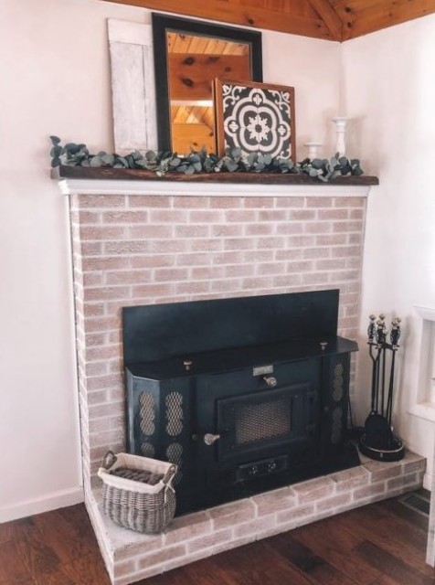 a beautiful whitewashed brick fireplace with a metal hearth, a walnut mantel and some greenery