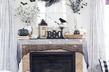 a black Halloween mantel with black cheesecloth, bats, branches, black and white pumpkins, lanterns and blackbirds