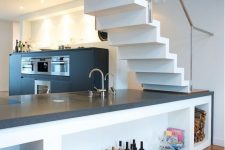 a black modern kitchen with a kitchen island placed under the stairs, with storage compartments and lights