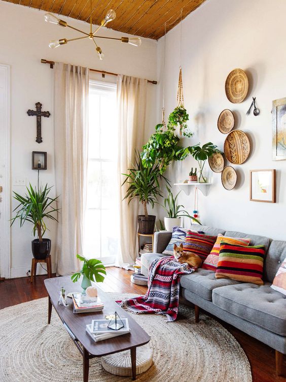 a boho living room with a grey sofa and bright pillows, a coffee table, decorative baskets, artwork, greenery and a rug