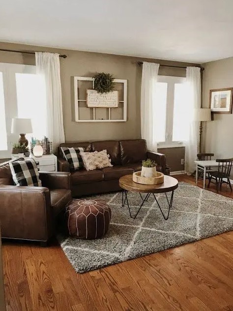 a boho rustic living room with brown leather seating furniture, a hairpin leg table, a brown leather pouf, some shabby chic decor