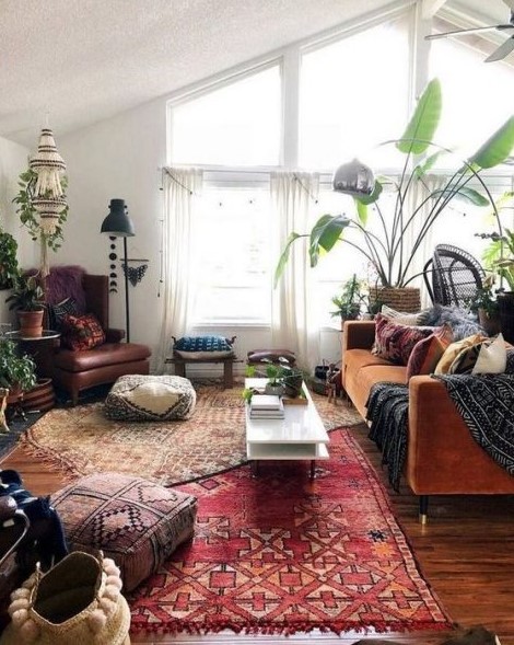 a boho space with a rust velvet sofa, boho rugs and ottomans, floor lamps and potted plants