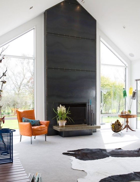 A bold light filled living room with a fireplace clad with blackened steel sheets and with a bright leather chair in front of it