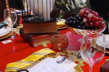 a bright Harry Potter themed tablescape done in red and gold, with an owl, gruit in a bowl and some gold chargers