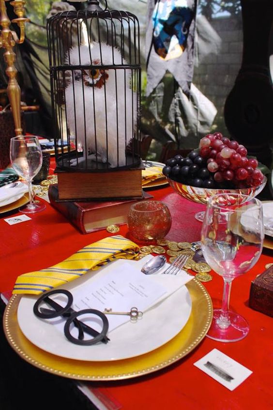 a bright Harry Potter themed tablescape done in red and gold, with an owl, gruit in a bowl and some gold chargers