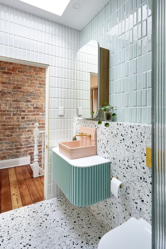 A bright bathroom with mint tiles, white terrazzo, a mint colored vanity, a pink sink and a mirror cabinet