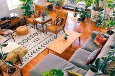 a bright boho living room with a grey sectional, a coffee table, mustard chairs and a yellow sofa, a lot of plants and some stools