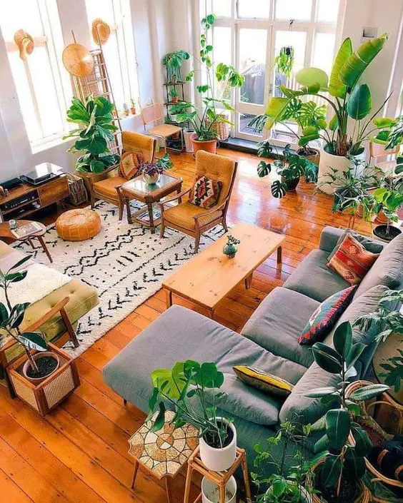 a bright boho living room with a grey sectional, a coffee table, mustard chairs and a yellow sofa, a lot of plants and some stools