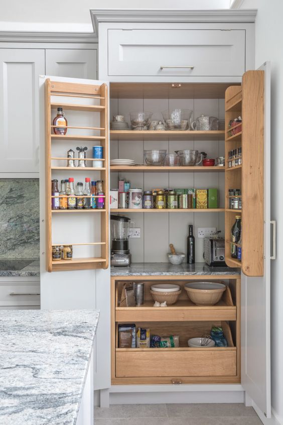 a built-in pantry that perfectly matches the cabinets, with stained drawers and shelves, some tableware, cookware, oils and spices