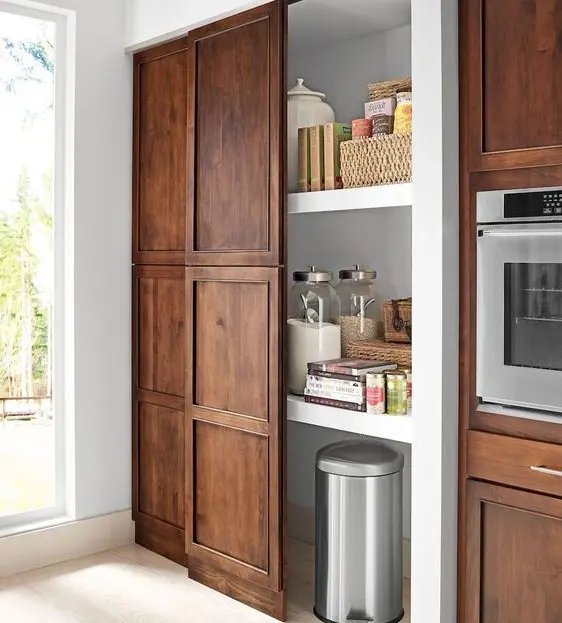 a built-in pantry with a sliding traditional door that matches the whole kitchen design is a cool idea