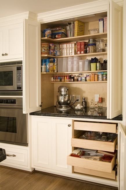 a built-in pantry with open shelves that hold food, spices, some appliances and additional drawers below