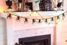 a catchy Halloween mantel with a spider garland, lights, branches with leaves, a scary house and some pumpkins on the floor