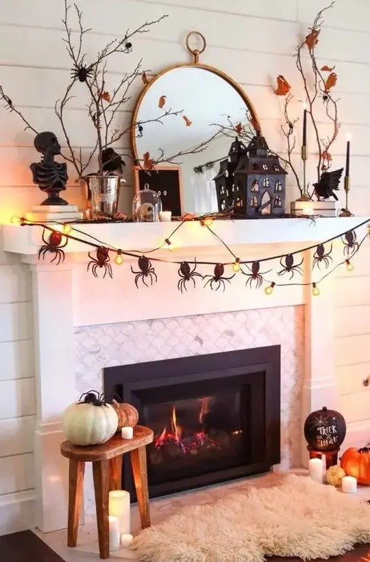 a catchy Halloween mantel with a spider garland, lights, branches with leaves, a scary house and some pumpkins on the floor