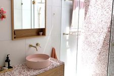 a catchy modern bathroom with a shower and a skylight, a stained vanity, pink terrazzo, a pink sink and a mirror cabinet