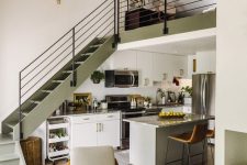 a catchy space with an olive green stairscase, cabinets and a grey kitchen island, stone countertops and built-in lights