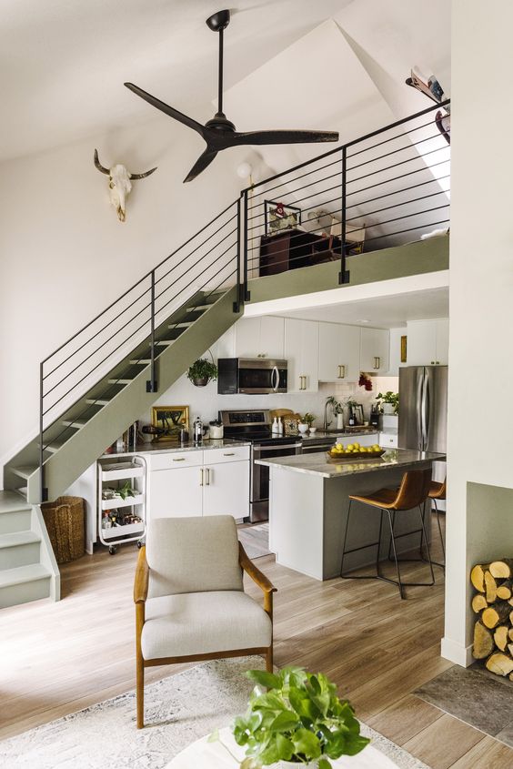 A catchy space with an olive green stairscase, cabinets and a grey kitchen island, stone countertops and built in lights