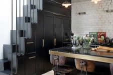 a catchy vintage kitchen in black with cabinetry built into the staircase, a large table that is a kitchen island and vintage decor
