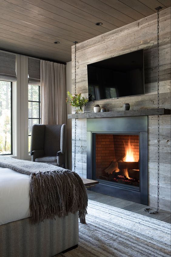 a chalet bedroom clad with reclaimed wood, a metal fireplace, a TV, a mtnel on chain and some comfy furniture