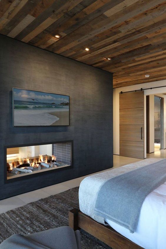 A chalet fireplace witha reclaimed wood ceiling, a bed, a double sided metal clad fireplace and some artwork