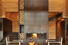 a chalet space with a lage metal clad fireplace with firewood storage, a couple of chairs, side tables and some lights
