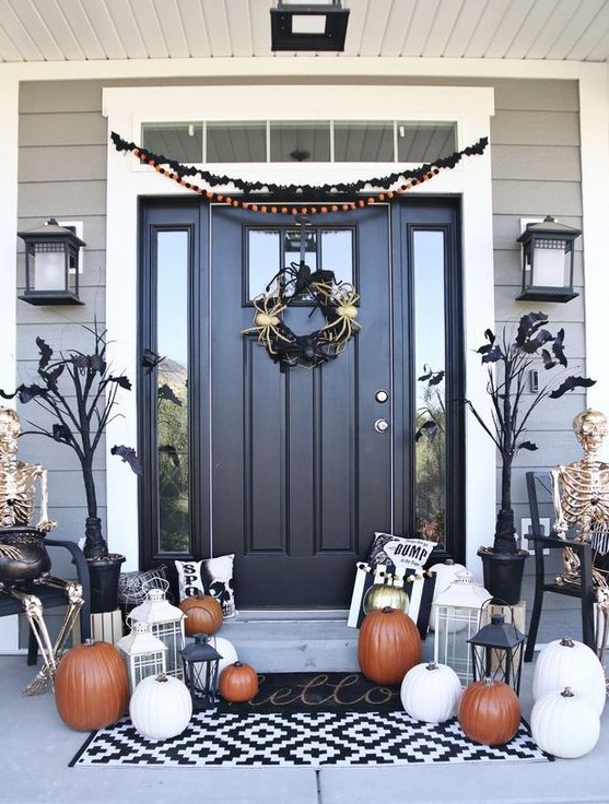 a chic classic Halloween porch with black trees with bats, a spider wreath, white, orange and gold pumpkins and lanterns