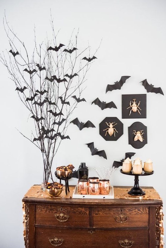 a chic dessert table with lots of bats around, gold bugs on the wall and copper mugs is ideal for Halloween