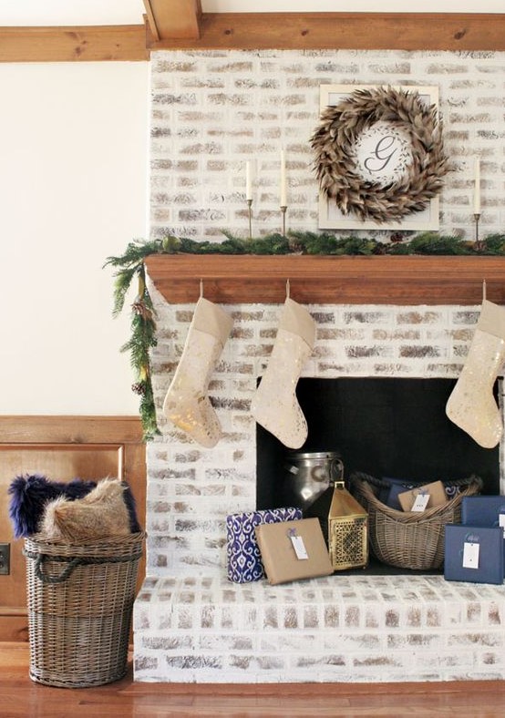 a chic whitewashed brick fireplace with a wooden stained mantel, baskets, candle lanterns and stockings for Christmas