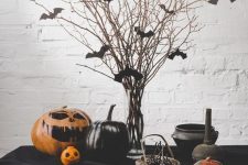 a classic Halloween table setting with bats on branches, black pumpkins and a painted orange one, a black tablecloth